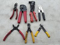 Seven assorted hand tools arranged flat showing varying handle colors and tool types like pruners, wire cutters, and crimpers