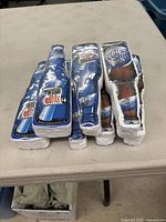 Seven vacuum-packed t-shirts in bottle-shaped packaging resembling Labatt Blue Light beer bottles.