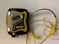 Front of Sony Sports Walkman portable cassette player with yellow accent and attached yellow wired earbuds.