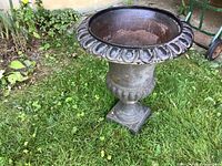 Front view of the vintage cast iron urn on grass, showing decorative rim and pedestal base.