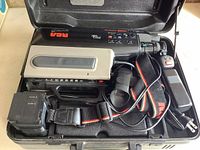 Vintage black and silver RCA Pro Color VHS camcorder with shoulder strap, battery pack, and power cord inside black hard plastic RCA case.