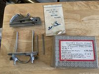 Complete set of Record 043 plough plane parts placed on wooden table including main body, adjustable fence, cutters, original box, and instruction manual.
