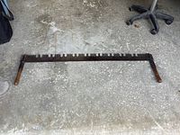 Full view of vintage two-man saw laid on concrete floor showing steel blade with wooden handles at both ends