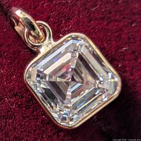 Front view of pendant showing square step-cut diamond in bezel setting against red background