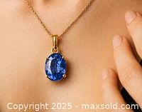 The pendant worn around a person's neck showing the deep blue oval tanzanite gemstone in a 14k yellow gold setting.