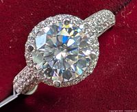 Close-up of 925 silver ring featuring large round 2ct Moissanite with halo and pave-set stones on the band against red background.