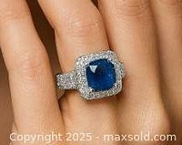 Front view of ring on finger showing blue cushion cut sapphire with halo of smaller stones.