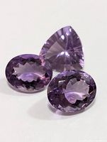 Three amethyst gemstones displayed on a white background, showing their faceted cuts and purple color.