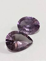 Photo showing two faceted amethyst gemstones, one oval and one pear-shaped, highlighting their clarity and color.