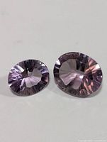 Two genuine amethyst gemstones placed on a white background, different sizes, showing faceted cuts and light purple color.