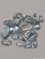 Close-up of multiple genuine aquamarine gemstones in various shapes and cuts showing light blue color and clarity.