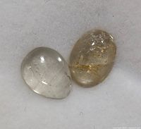 Close-up view of two polished Zultanite cabochon stones showing color and inclusions on white background.
