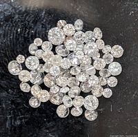 Close-up photo of loose diamonds scattered on black fabric showcasing their varying sizes and round brilliant cuts.