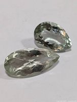 Two faceted pear-shaped green amethyst gemstones on a white background, clear light green color, polished and transparent.
