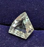 Top view of a light green amethyst gemstone with faceted kite-like pentagonal shape on dark fabric background.