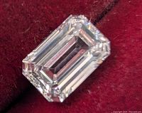 Loose emerald cut lab created diamond on red velvet background, top view