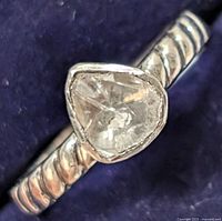 Close-up photo of the silver ring showing the roughly triangular diamond and textured band against a dark blue background.