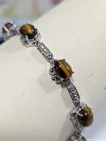 Close-up showing tiger eye stones set in sterling silver claw prong settings with small clear stones on silver links.