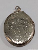 Front face of the large oval silver locket pendant showing floral and leaf engraving pattern