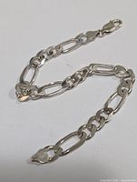 Close-up of 9-inch sterling silver chain bracelet with lobster clasp laid flat showing link design and clasp detail.