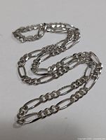 Close-up of the entire silver figaro chain necklace laid out on a white background showing the link pattern and overall condition.
