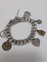 Silver charm bracelet laid flat showing chain link design and attached charms including religious medals and heart charm.