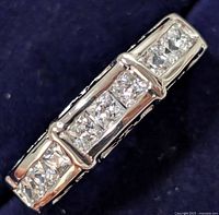 Close-up front image of silver ring showing three segments of square-cut cubic zirconia stones set flush in the band.