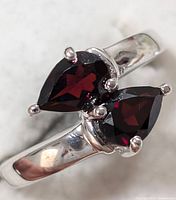 Close-up view of ring's front showing two pear-shaped deep red garnet stones in silver prong setting with polished silver band.