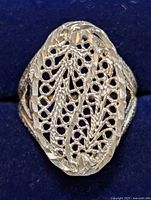 Close-up of silver filigree ring on dark blue fabric background showing intricate leaf and vine cut-out design on oval top.