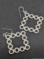 Close-up front view of both silver earrings showing circular hollow link design in a diamond shape on black background.