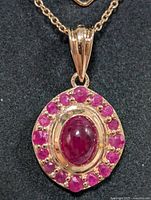 Close-up photo of pendant front showing central oval cabochon ruby surrounded by smaller faceted rubies in silver setting.