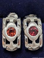 Front view of pair of sterling silver earrings with red gemstones in floral bezel, showing design and stone color clearly.
