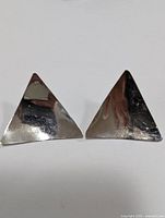 Pair of triangular silver earrings laying flat, showing their shiny polished surface and triangular geometric shape.