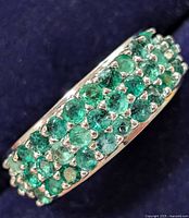 Close-up photo showing side angle of silver ring with three rows of round green emeralds.