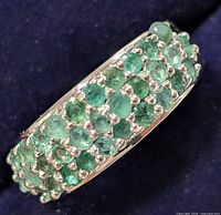 Close up of silver emerald ring showing three rows of round-cut emerald stones on the band
