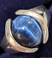 Close-up image showing silver ring with central blue cat's eye gemstone, highlighting bezel setting and gemstone chatoyancy.