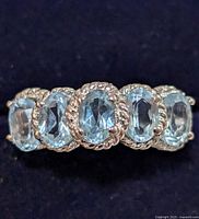 Close-up front view of the silver ring showing five oval light blue topaz stones with a detailed twisted rope bezel setting.