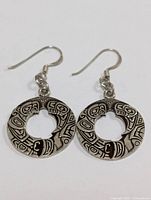Front view of one silver earring showing circular shape and detailed tribal-inspired engravings with fishhook wire.