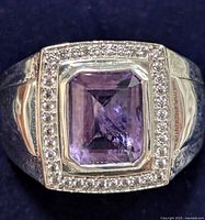 Close-up of rectangular-cut purple amethyst in silver ring with clear stones border on broad band.