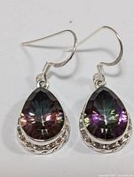 Front view of the pair of silver earrings with pear-shaped mystic topaz stones and decorative bezel setting.