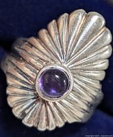 Close-up photo of the ring showing the textured silver design and round amethyst gemstone on a dark blue background.