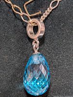 Close-up of the silver chain and blue topaz teardrop pendant showing detail of faceted gemstone and silver bail.
