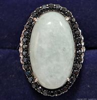 Top view showing large oval light green jadeite stone surrounded by black onyx stones in polished silver setting