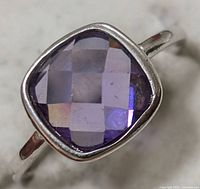 Close-up front and angled views of a silver ring featuring a square cushion-cut amethyst stone with faceted surface. The ring is size 5, with a simple bezel setting and slim band.