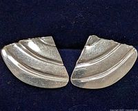 Top-down photo showing the pair of silver earrings with curved decorative stripes on a dark background.