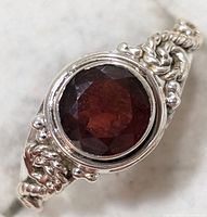 Close-up front view of the silver garnet ring showing the deep red faceted garnet and detailed silver band design.