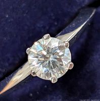 Close-up photo of silver ring with round-cut moissanite gemstone on a deep blue background