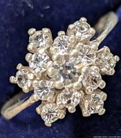 Close-up of silver ring with cluster of clear crystals showing flower-like design.