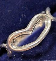 Close-up of silver ring showing hollow open heart shape design at center on dark fabric background.