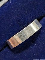 Side angle of a plain silver band ring showing surface texture and light scratches.